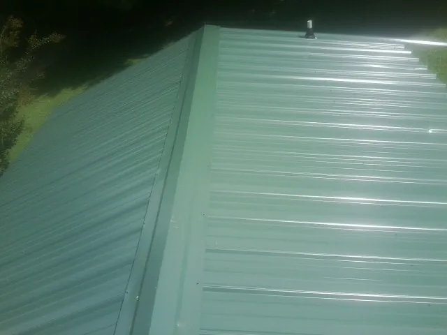 New green metal panels meeting at the ridge of a roof — Flat Roof Repair work by our crew in Wayland