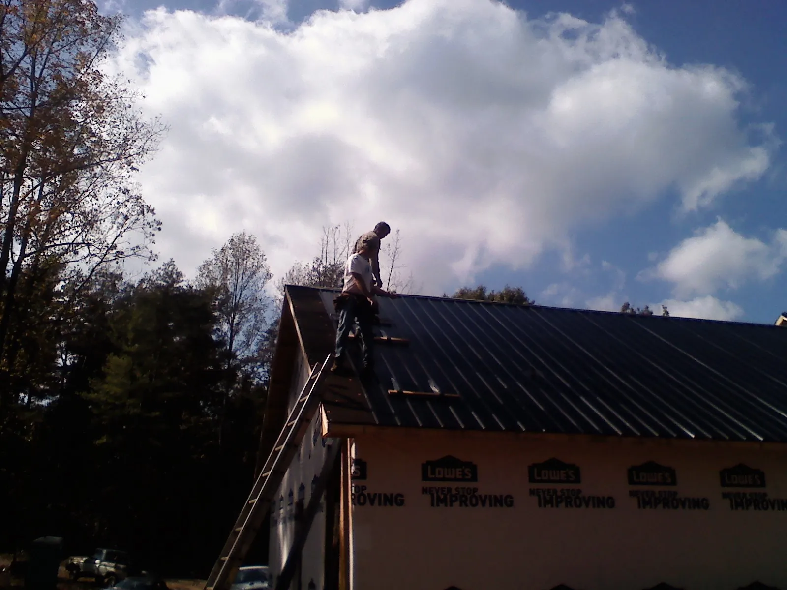 Roofer fastening dark metal panels high against a cloudy sky, from a Roof Inspection job in Wayland