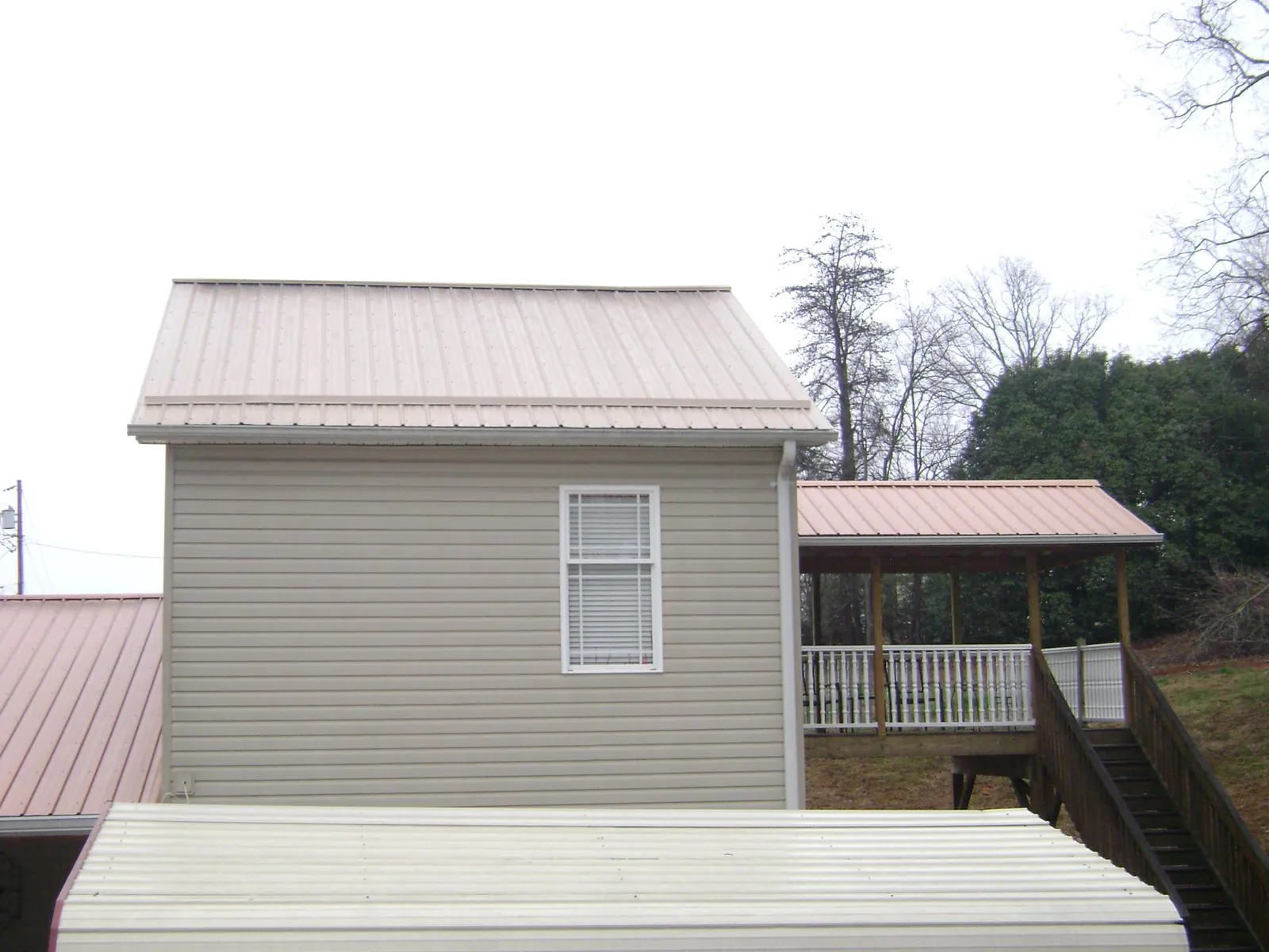 Tan metal roofs on a two story addition and attached porch, from a Roof Replacement job in Wayland